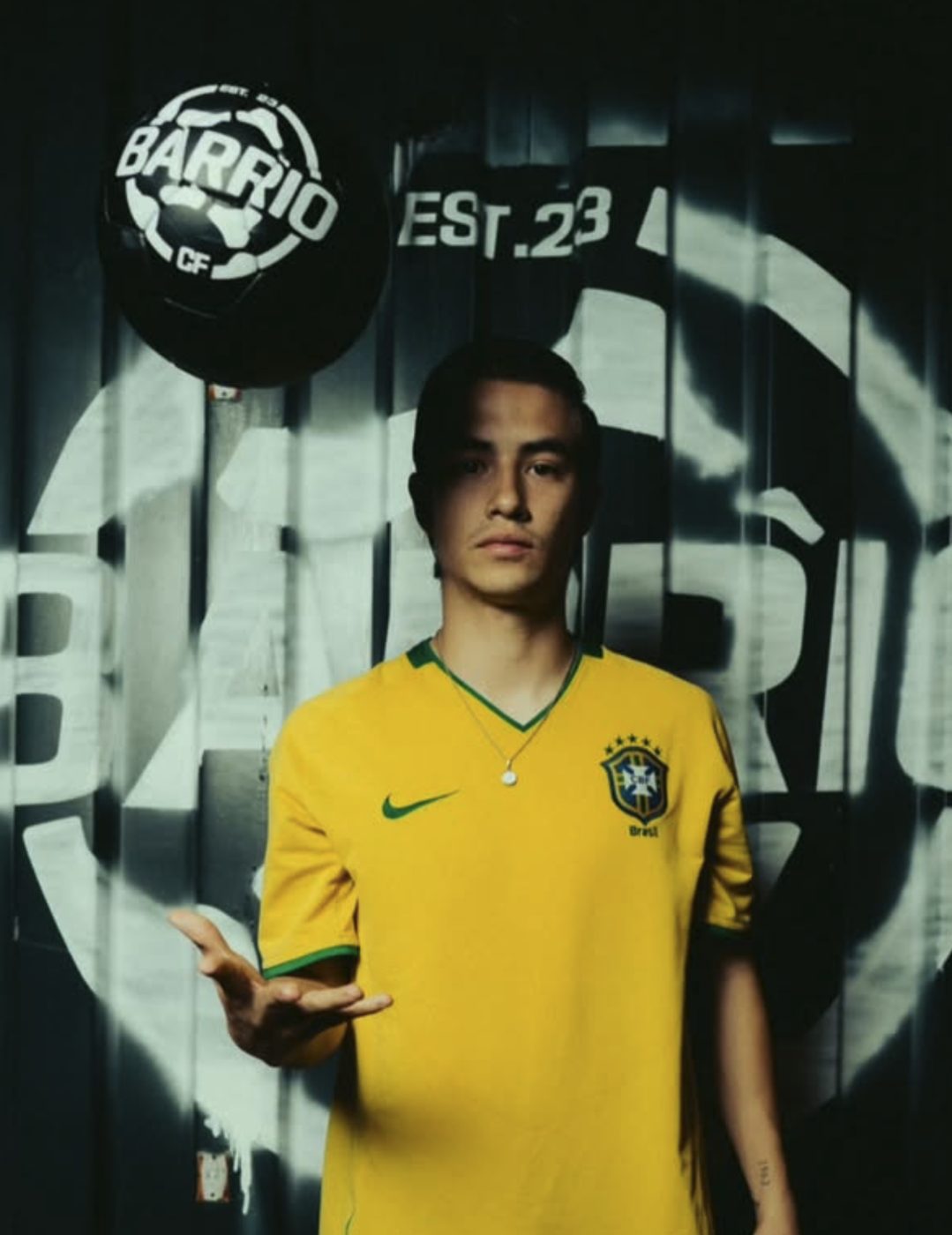 A player in a yellow jersey tossing a Barrio football in front of the club mural